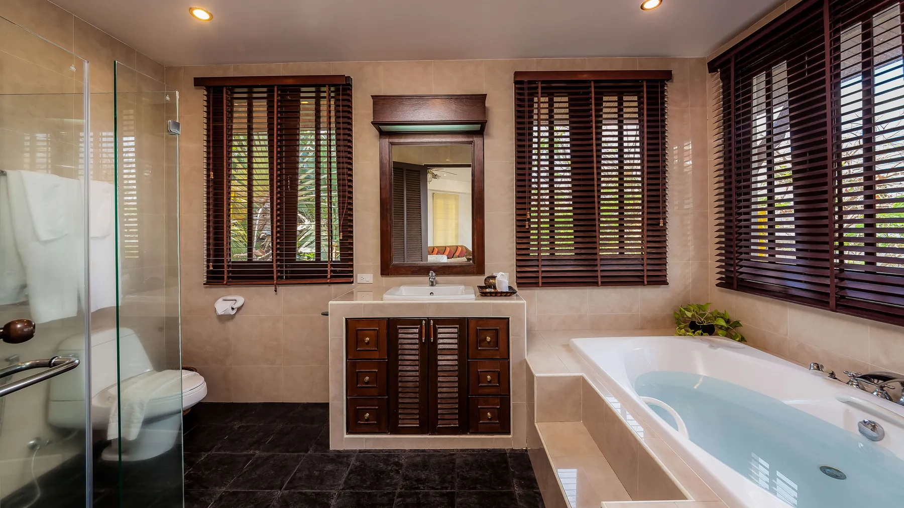 An ensuite spa bath framed by timber shutters, with a glass shower alongside