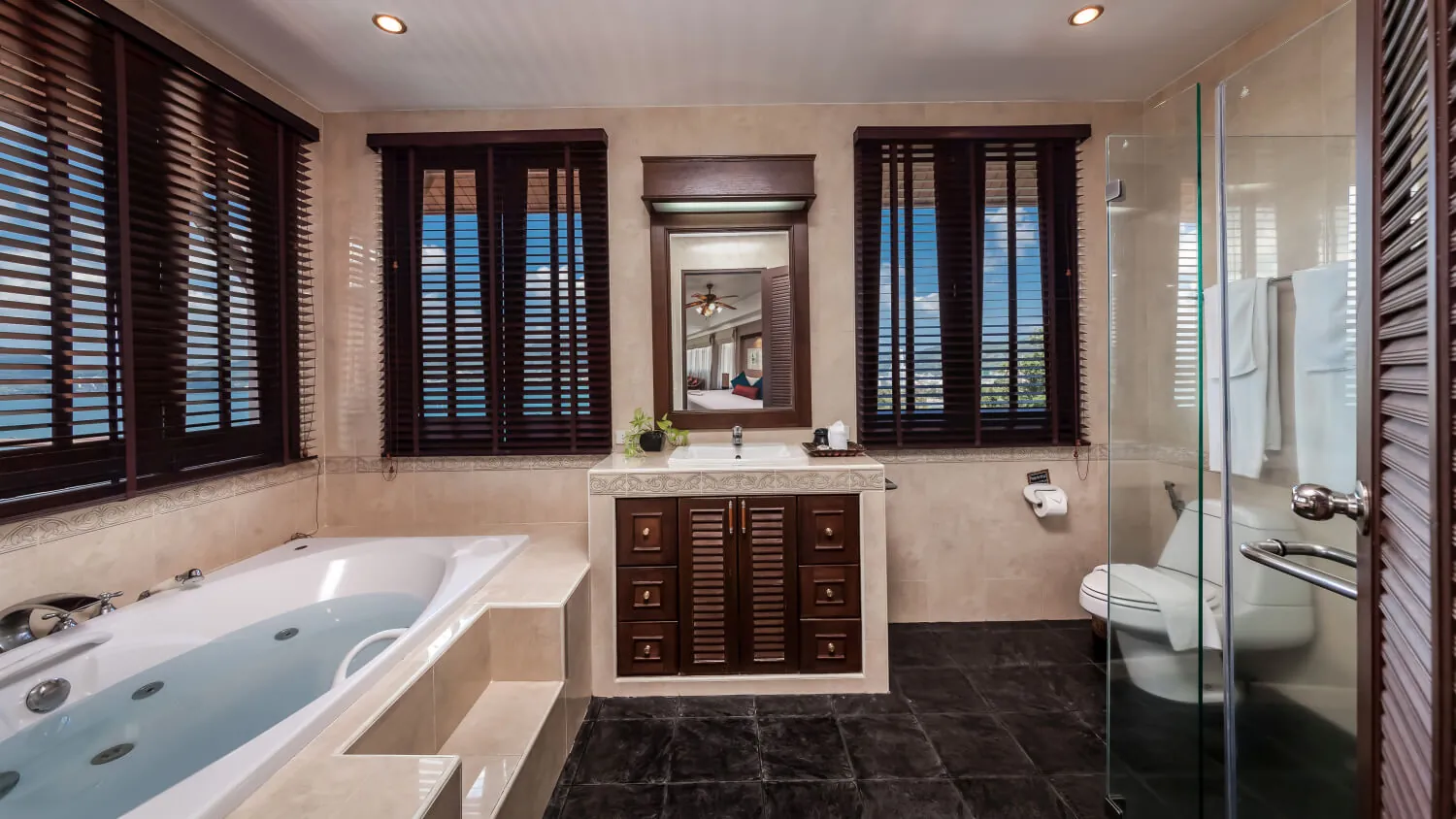 An ensuite bathroom at Villa Baan Paradise with a spa bath set under timber shutters and a walk-in shower