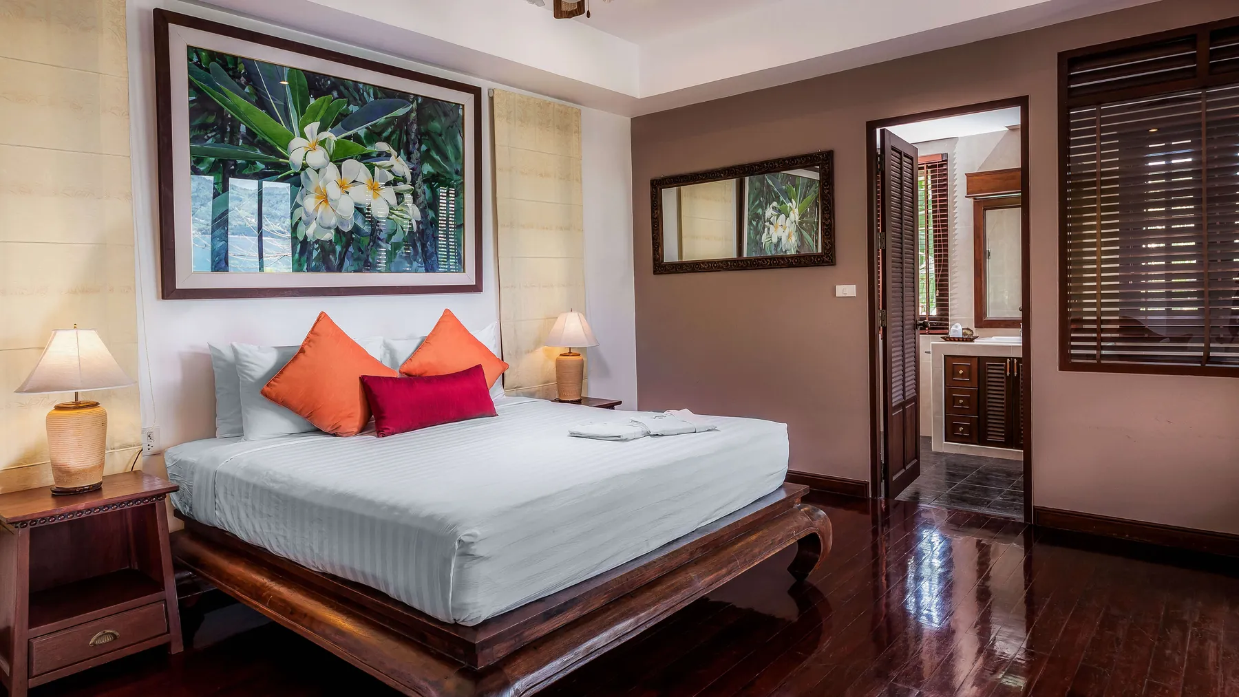A king bedroom on dark timber floors, framed artwork above the bedhead and an ensuite alongside