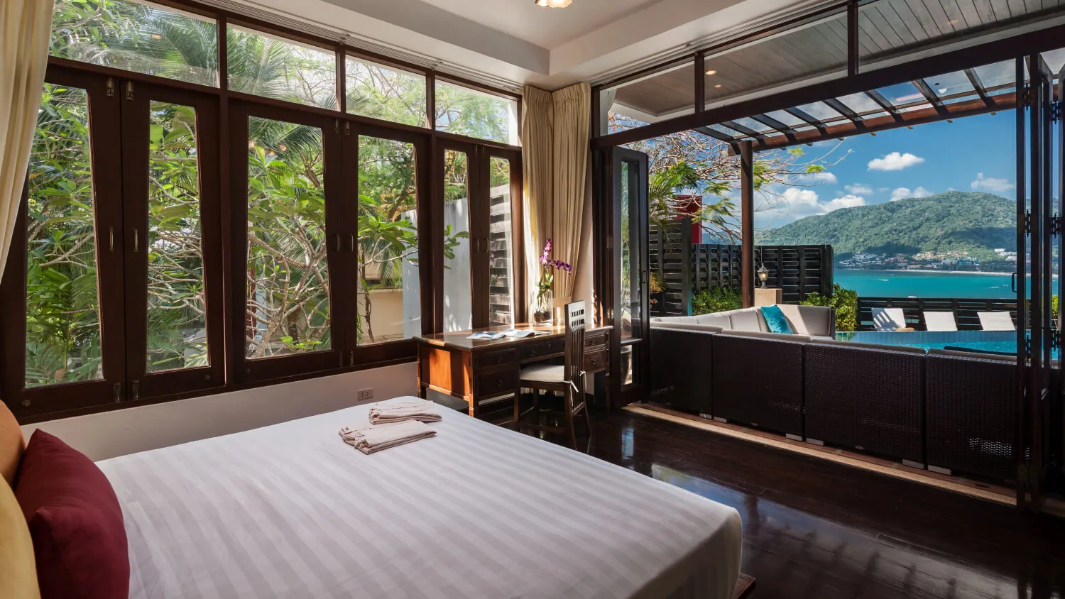 A bedroom wrapped in dark-framed windows looking into the jungle, the bed turned down with fresh towels