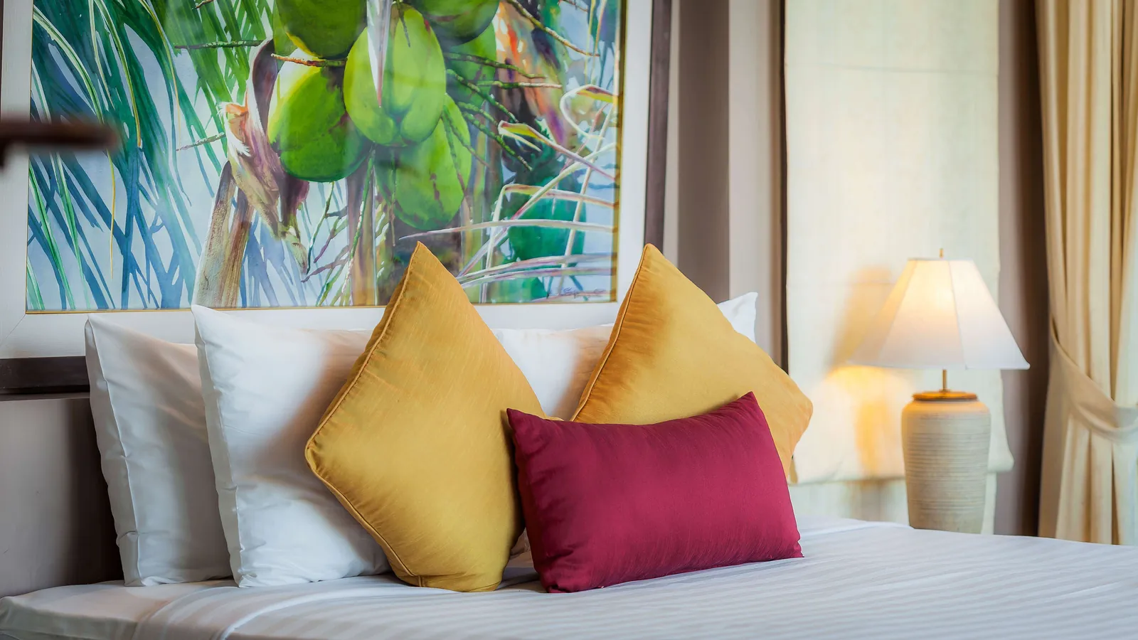A bed dressed with gold and burgundy cushions in front of a tropical mural