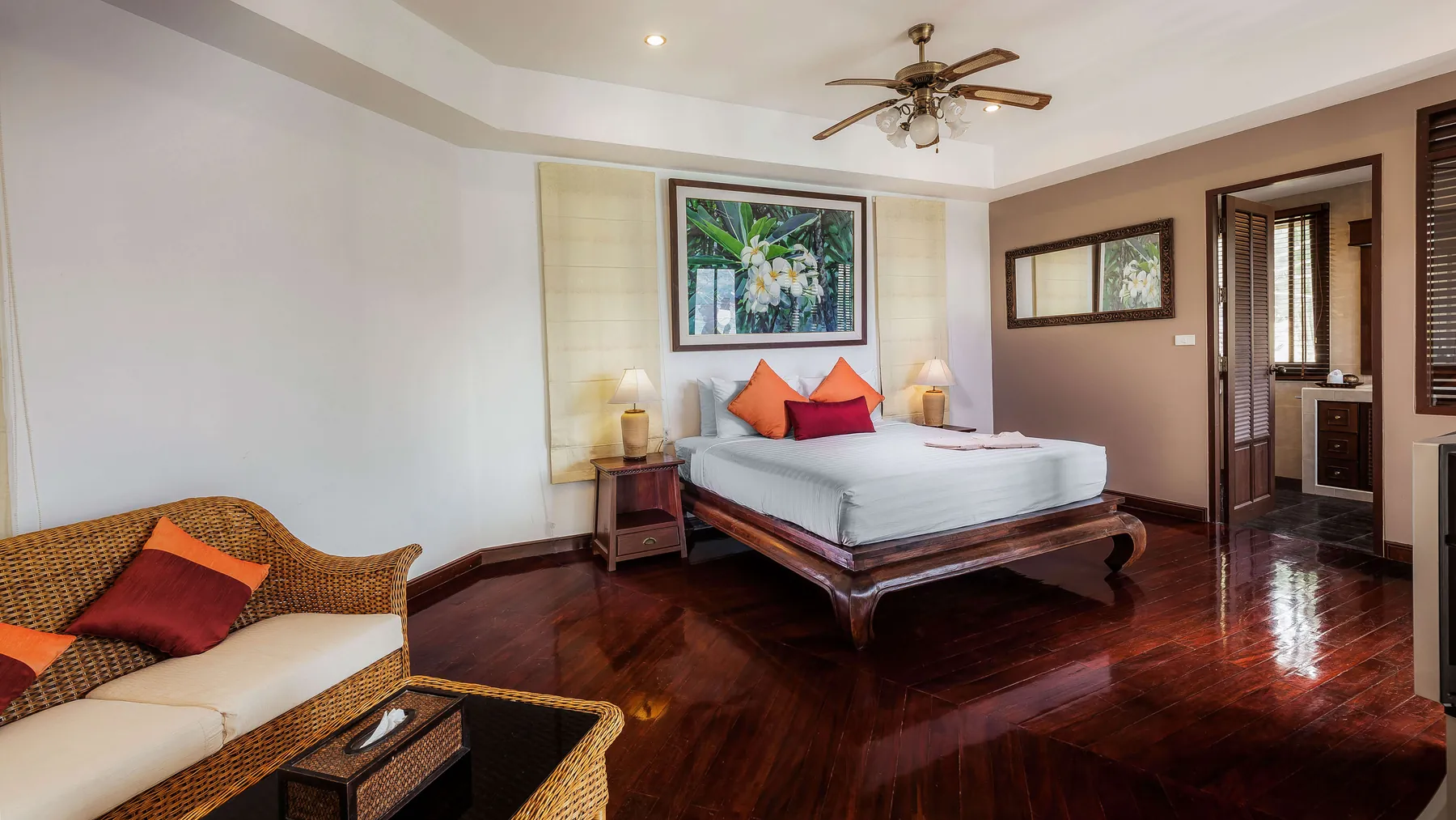 A bedroom with its own sofa and armchair, a ceiling fan and an ensuite through the doorway