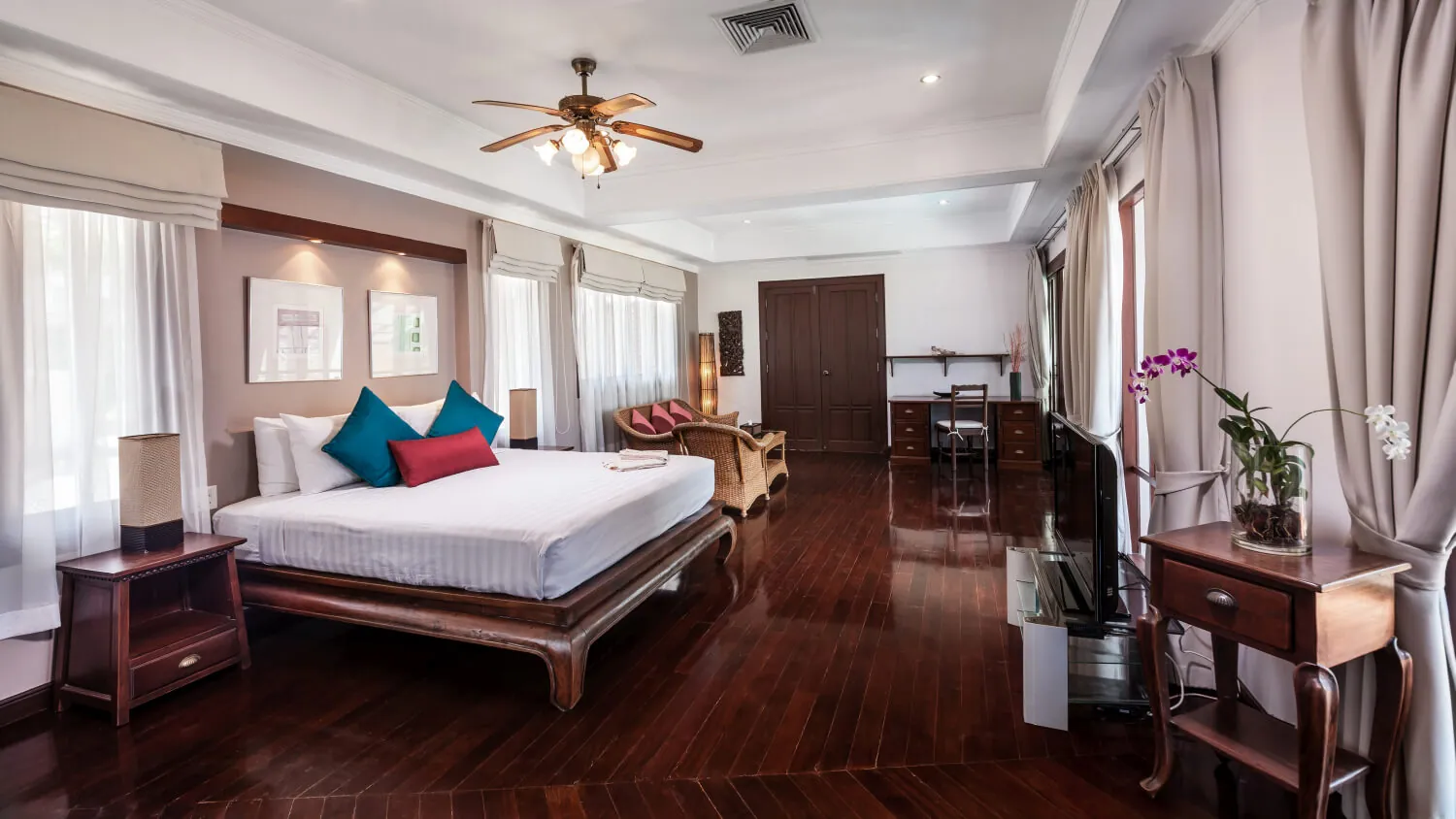 A king bedroom at Villa Baan Paradise with a ceiling fan, writing desk and an orchid on the side table