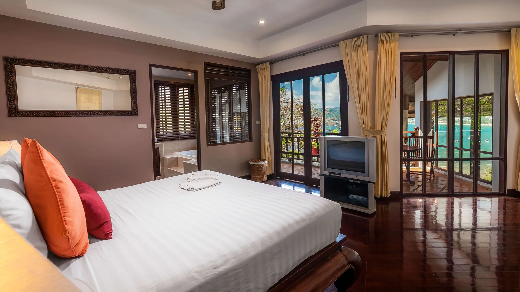A bedroom at Villa Baan Paradise with a television, curtained doors and a glimpse of the sea