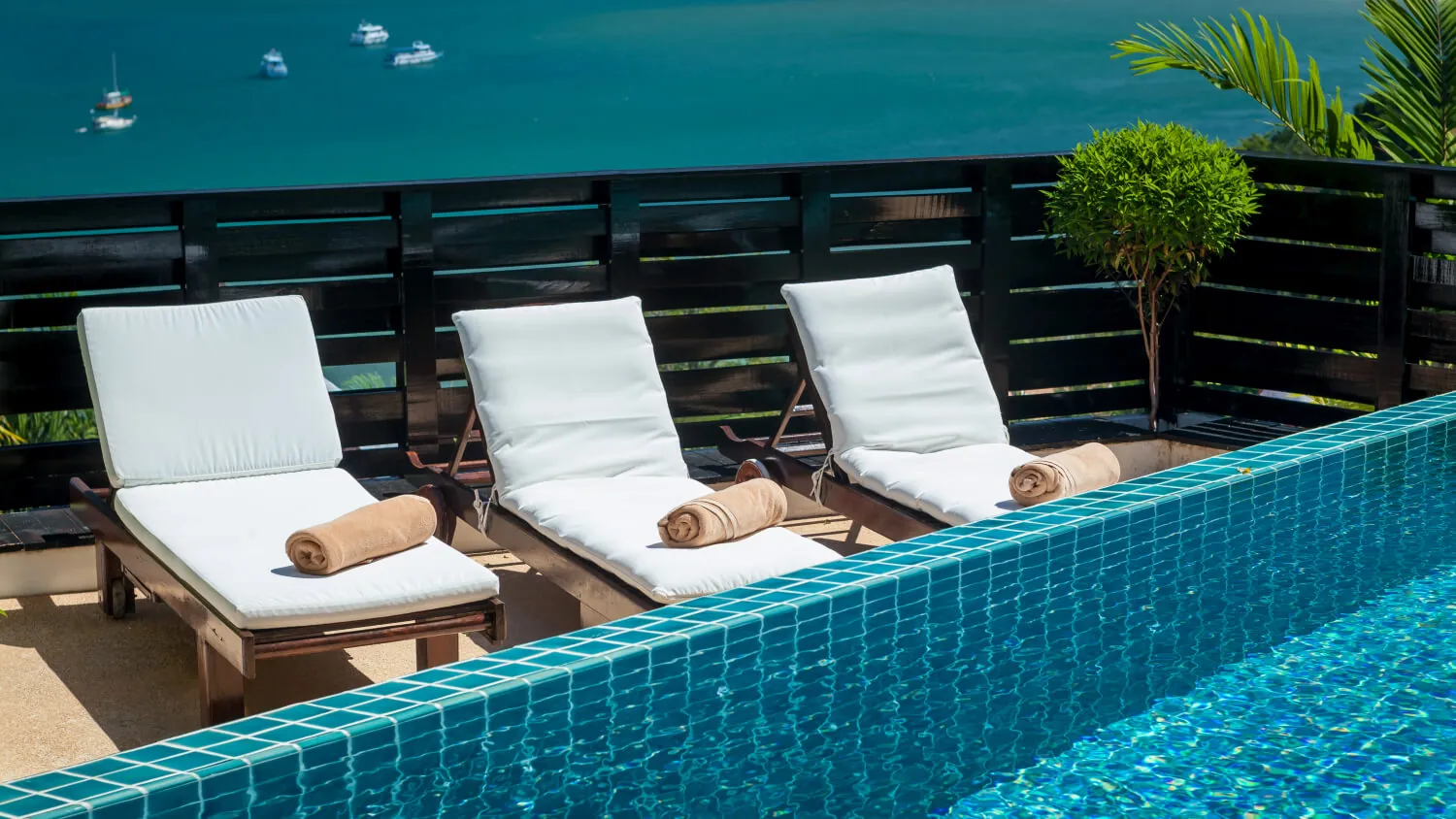 Three sun loungers with rolled towels on the pool terrace above Patong Bay