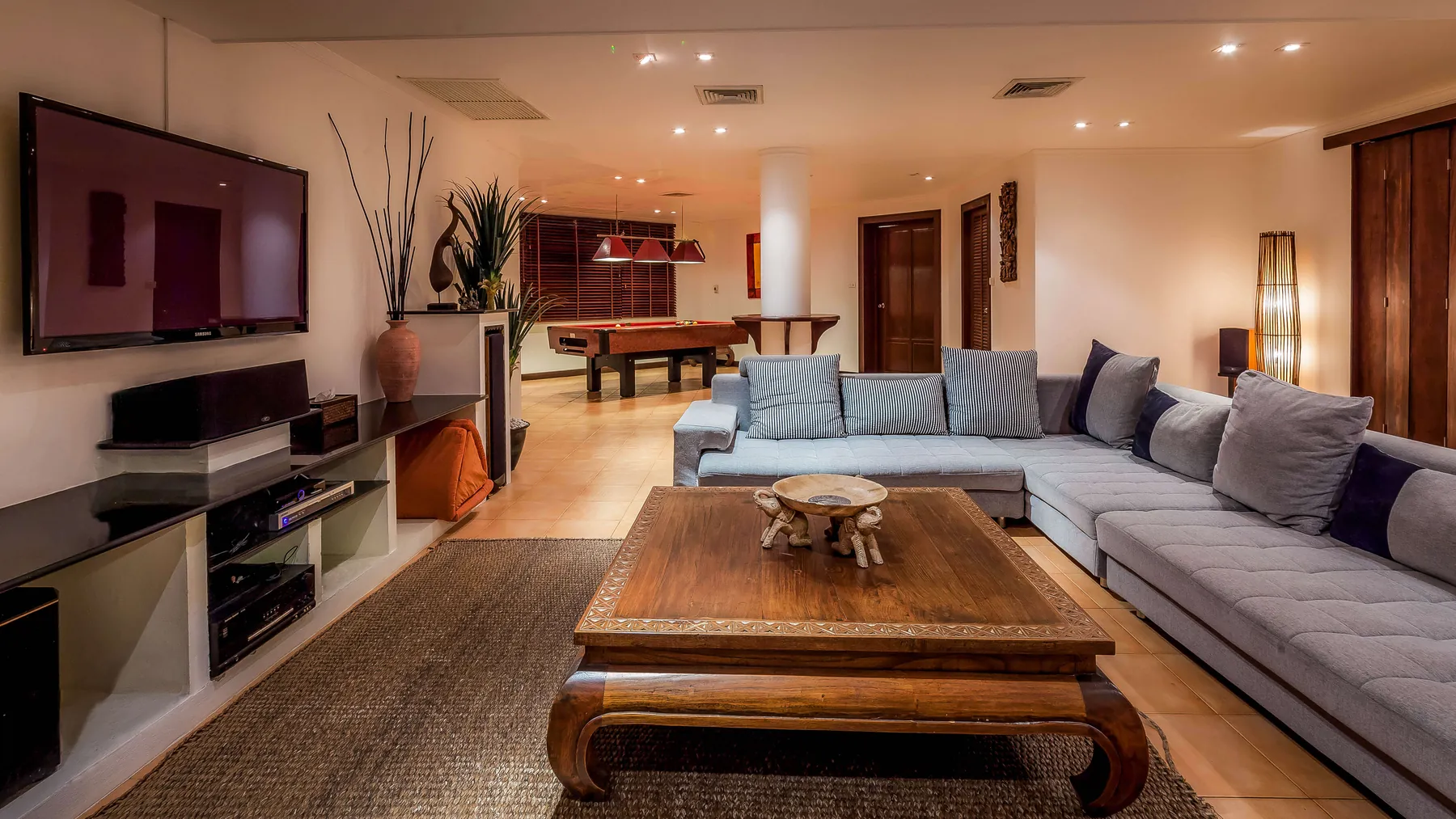 The downstairs media room with its wall-mounted television, sectional sofa and the pool table beyond