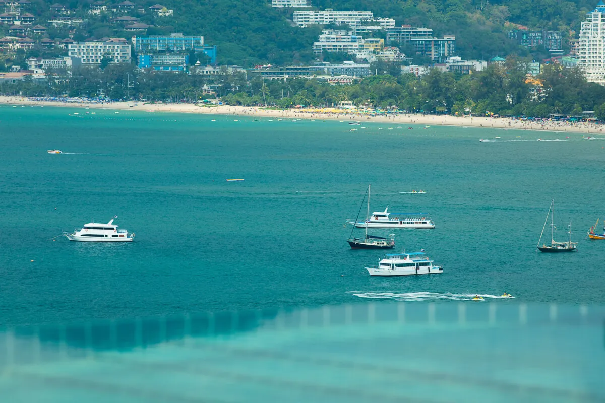 The turquoise water of Patong Bay with longtail boats moored off the beach and the town and hills behind