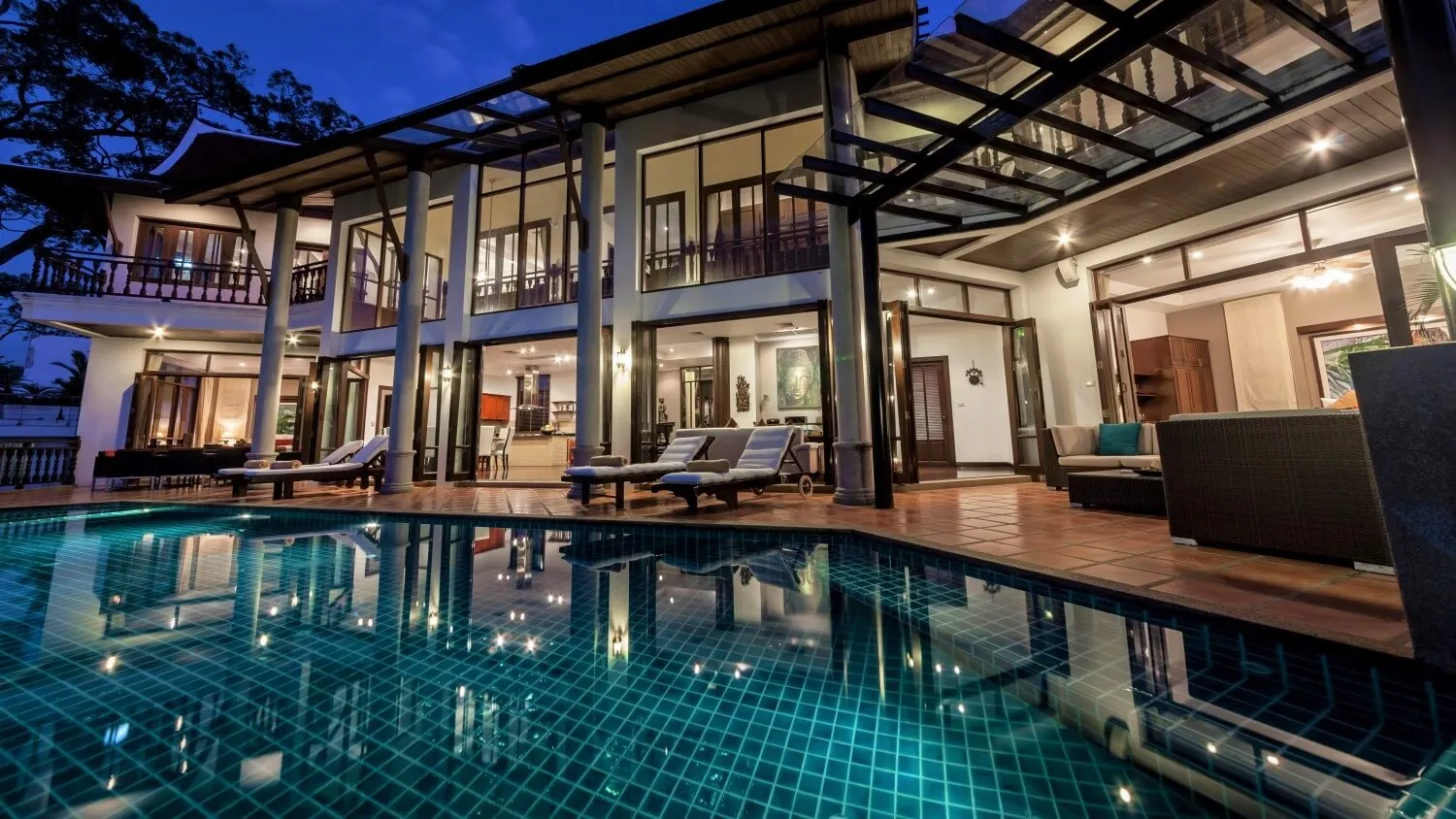 The two-storey open living pavilion at night, reflected in the infinity pool