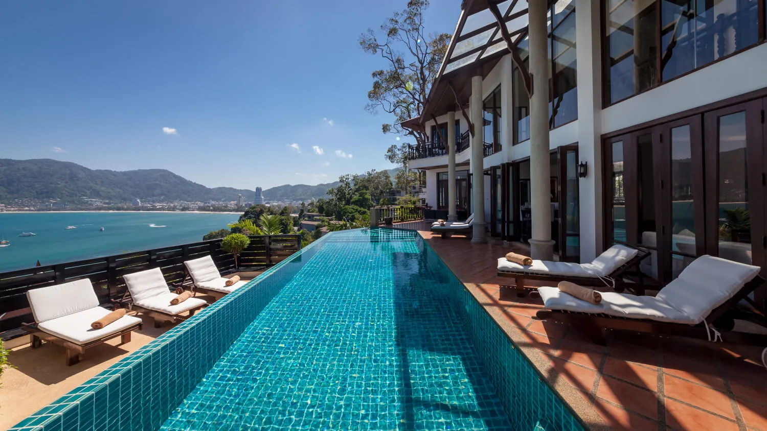 The infinity pool running the length of Villa Baan Paradise, with sun loungers on the terrace and Patong Bay beyond