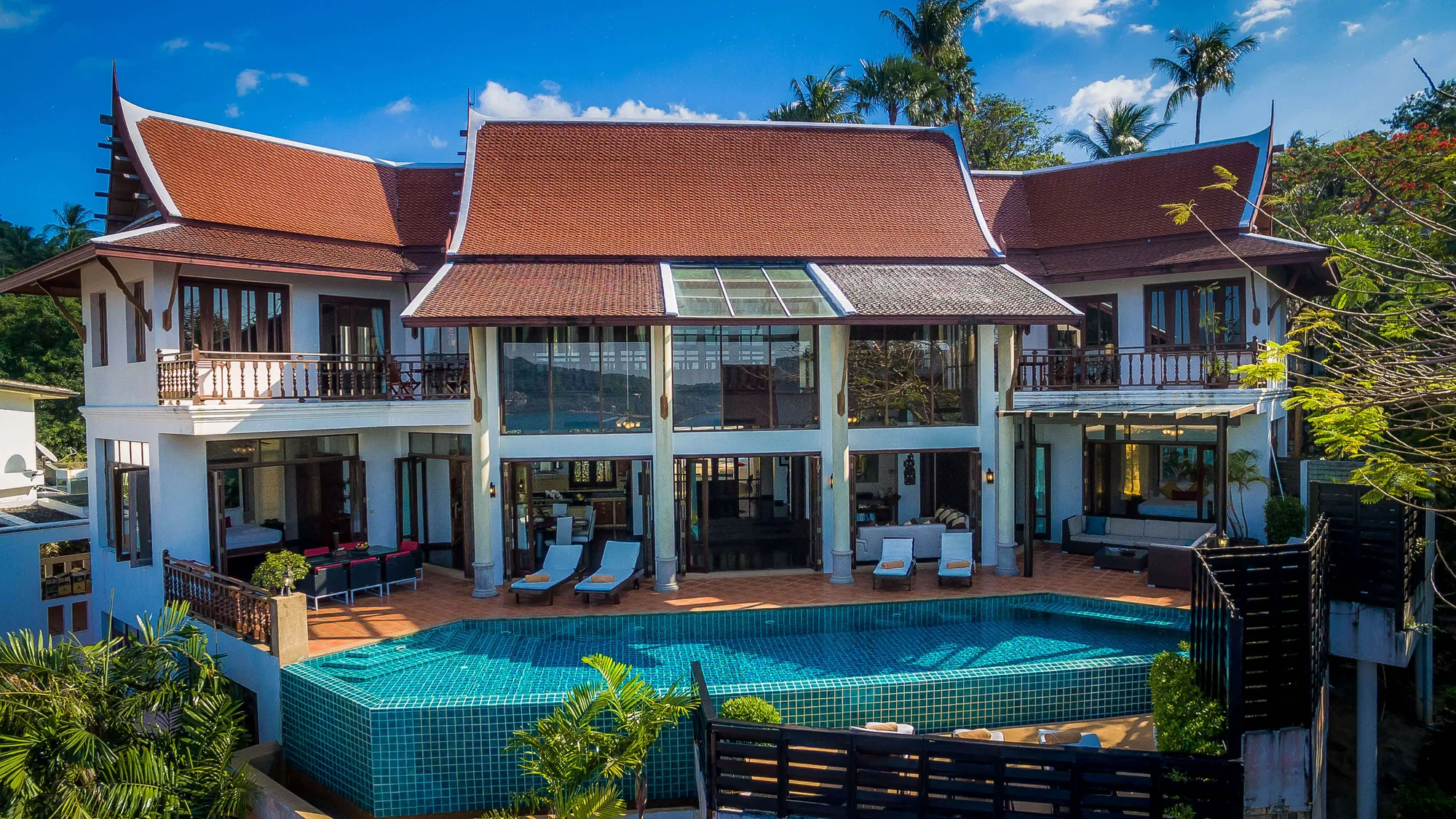 Villa Baan Paradise from the garden: the traditional Thai tiled roof, the glazed living pavilion and the turquoise pool